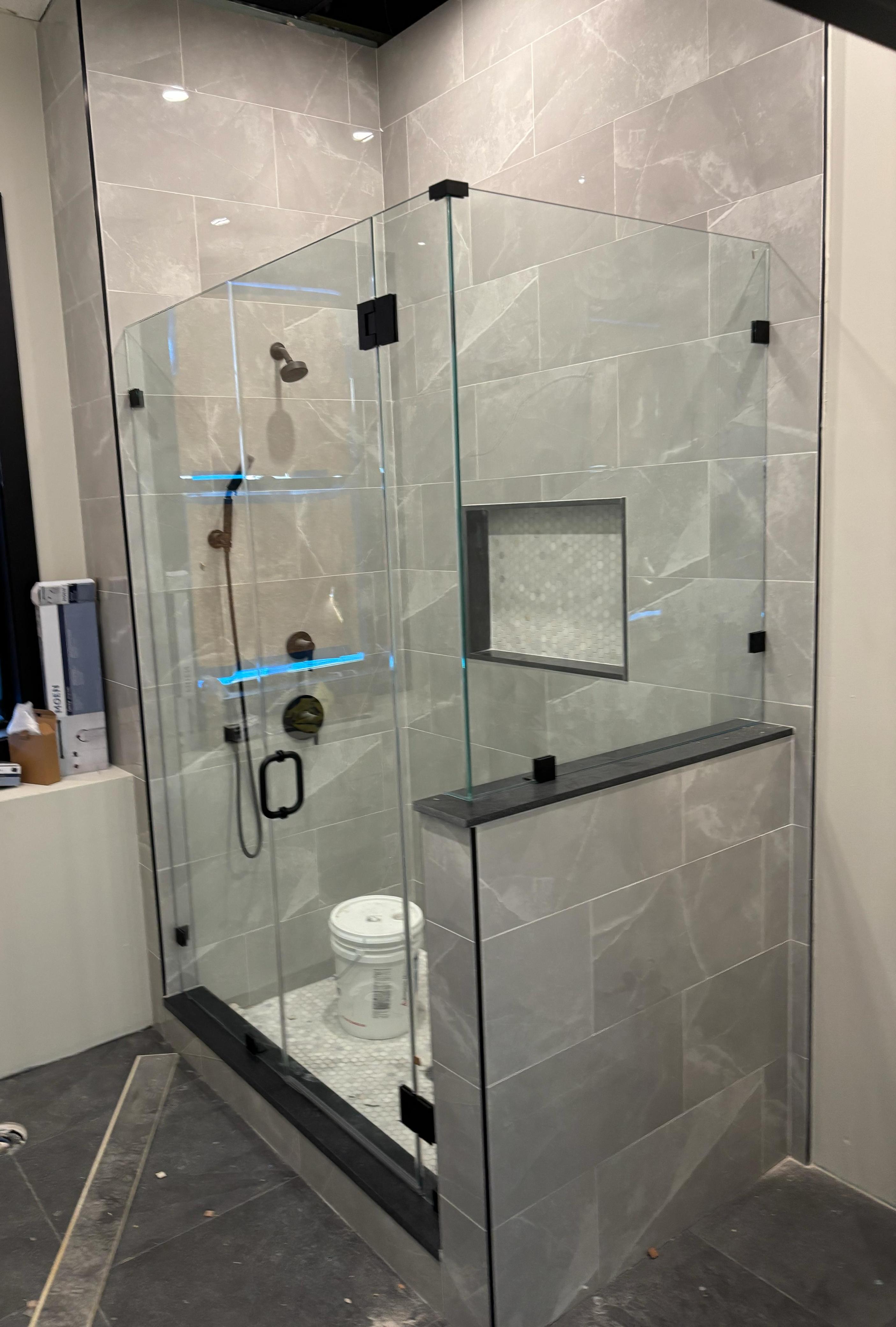 Custom glass shower enclosure with half wall and matte black clips in modern gray tile bathroom